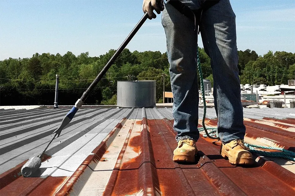 Rusted metal roof panels being rolled with primer before coating