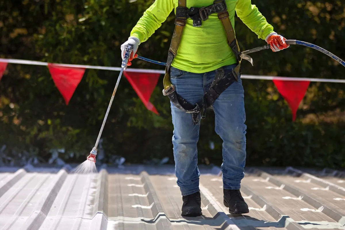 Roof coating being spray-applied over a commercial roof