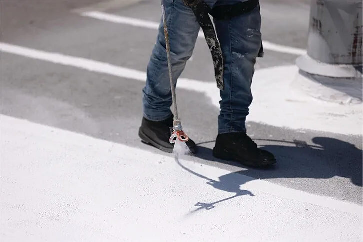 White silicone roof coating being spray-applied on a flat commercial roof