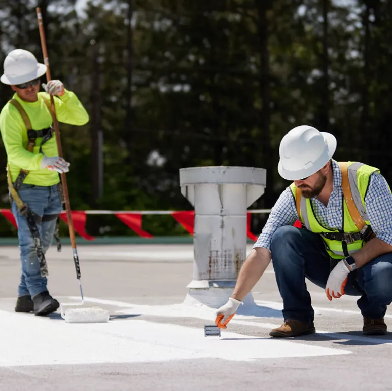 Roofers applying silicone coating around a rooftop vent